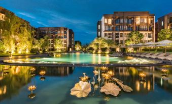 a large swimming pool with a few water lilies floating in the water , surrounded by buildings and lit up at night at Divalux Resort and Spa Bangkok, Suvarnabhumi Airport-Free Shuttle