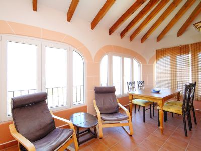 a room with two wooden chairs and a dining table , surrounded by large windows and wooden beams on the ceiling at Joli Joli Photo