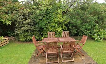 a wooden table and chairs set in a lush green garden , surrounded by trees and grass at Woodhouse Woodmancote