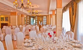 a large banquet hall with multiple dining tables set for a formal event , including white tablecloths , crystal glasses , and elegant decorations at Mon Port Hotel & Spa