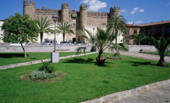 a large , grassy courtyard with palm trees and a building in the background , under a blue sky at Parador de Zafra