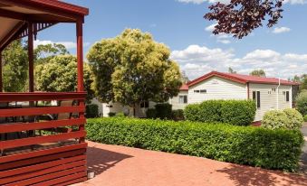 a red wooden gazebo in the middle of a green yard with trees and bushes at Nrma Dubbo Holiday Park