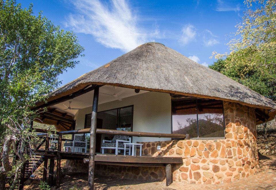 a small thatched - roof house with a stone facade and a wooden deck in front of it at Leopard Mountain Safari Lodge