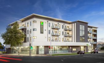 a modern apartment building with balconies and a green sign , situated on a street corner at Quest Werribee