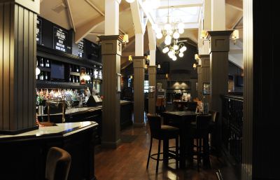 a bar with wooden tables and chairs , a chandelier hanging from the ceiling , and a large window at Village Hotel Liverpool