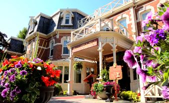 a large , red - brick building with a wooden porch and multiple flower pots , set against a clear blue sky at Prince of Wales