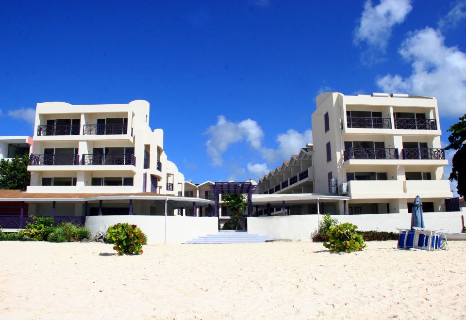 a beach scene with a large white building in the background , surrounded by sand and blue water at Infinity on the Beach