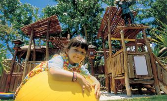 a young girl is playing with a yellow inflatable ball in a playground setting , surrounded by other children and adults at Shangri-Las le Touessrok Resort and Spa