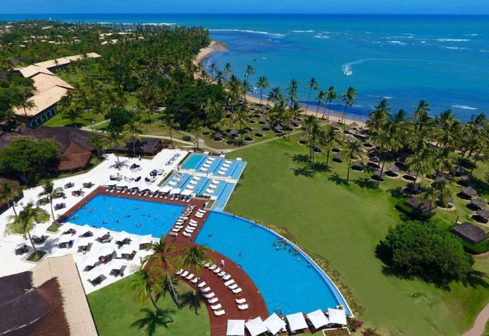 a resort with a large pool surrounded by lounge chairs and umbrellas , as well as a view of the ocean at Tivoli Ecoresort Praia do Forte