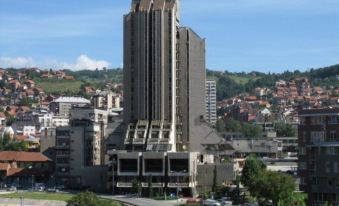 a tall , modern building with multiple stories and a distinctive spire is surrounded by trees and other buildings at Zlatibor Hotel