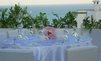 a dining table set with wine glasses and a vase of flowers , overlooking the ocean at La Villa Bleue-Sidi Bou Said