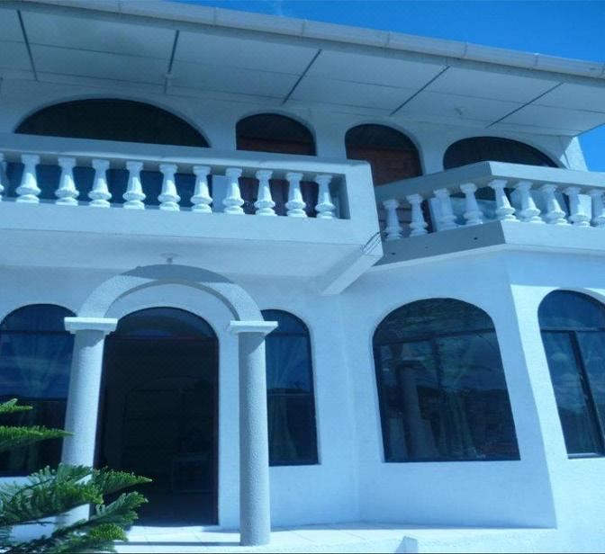 a white building with a balcony and columns is shown in the daytime light , set against a blue sky at Hotel El Castillo