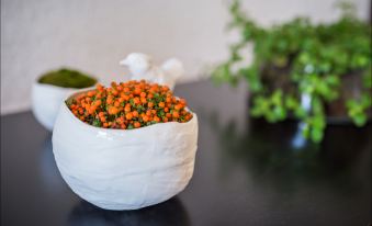 a white bowl filled with vibrant green and orange flowers is placed on a black table at Hotel Spa Azteca Barcelonnette