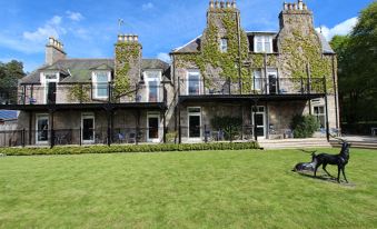 a large stone house surrounded by a lush green lawn , with several cars parked in front of it at Loch Kinord Hotel