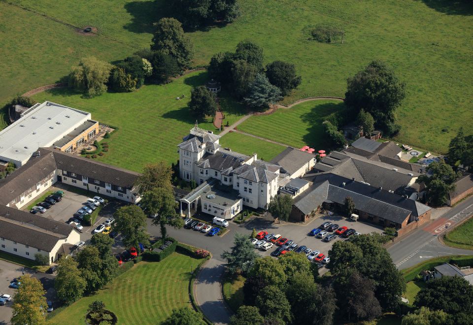 a large , well - maintained building with multiple floors and balconies , surrounded by green trees and grass , and surrounded by parking lots at Thornton Hall Hotel & Spa