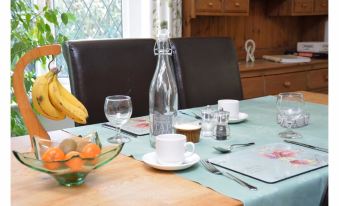 a dining table set with a blue tablecloth , silverware , and glasses , along with a bowl of fruit at Laburnum Cottage Guest House