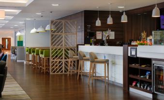 a modern , minimalist office interior with wooden floors , white walls , and green chairs around a wooden bar at Hampton by Hilton Exeter Airport