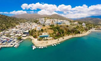 a picturesque coastal town with white buildings , blue water , and mountains in the background , under a clear blue sky at Minos Boutique Hotel