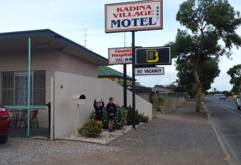 a man and a woman are standing next to each other in front of a building , with a sign on the side at Kadina Village Motel