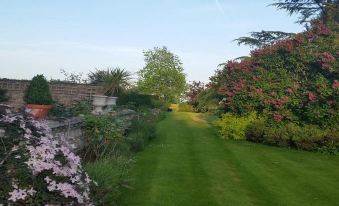 a lush green lawn surrounded by bushes and trees , with a fence surrounding the area at Blaisdon House B&B