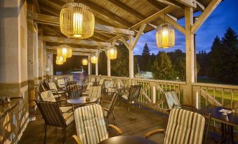 a wooden deck with outdoor seating , featuring striped chairs and hanging lanterns , under a wooden roof at Hotel Pod Lipou Resort