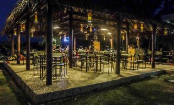 a nighttime scene of a restaurant with multiple tables and chairs , illuminated by lights , under a thatched roof at Shane Josa Resort