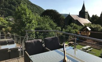 a rooftop patio with two dining tables and chairs , overlooking a beautiful mountain view and a church at Grapes Hotel, Bar & Restaurant Snowdonia Nr Zip World