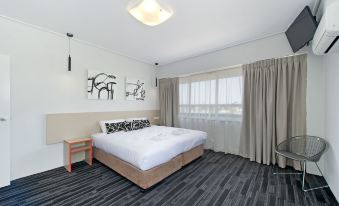 a large bed with white linens is situated in a room with gray carpeting and a window at Prince of Wales Hotel