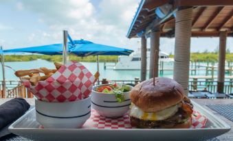 a burger , salad , and fries are served on a table near a body of water at Spanish Wells Yacht Haven