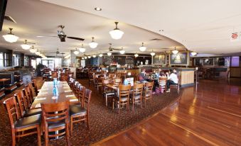 a large dining room with wooden tables and chairs , a bar area , and people seated at the tables at Wilsonton Hotel