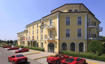 a large yellow building with balconies , surrounded by a parking lot filled with red cars at Maranello Palace Hotel