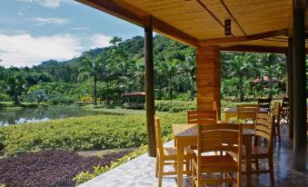 a wooden dining area with tables and chairs , surrounded by lush greenery and a pond at Macaw Lodge