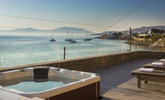 a deck overlooking the ocean , with a hot tub placed on the deck and boats docked nearby at Mykonos Beach Hotel