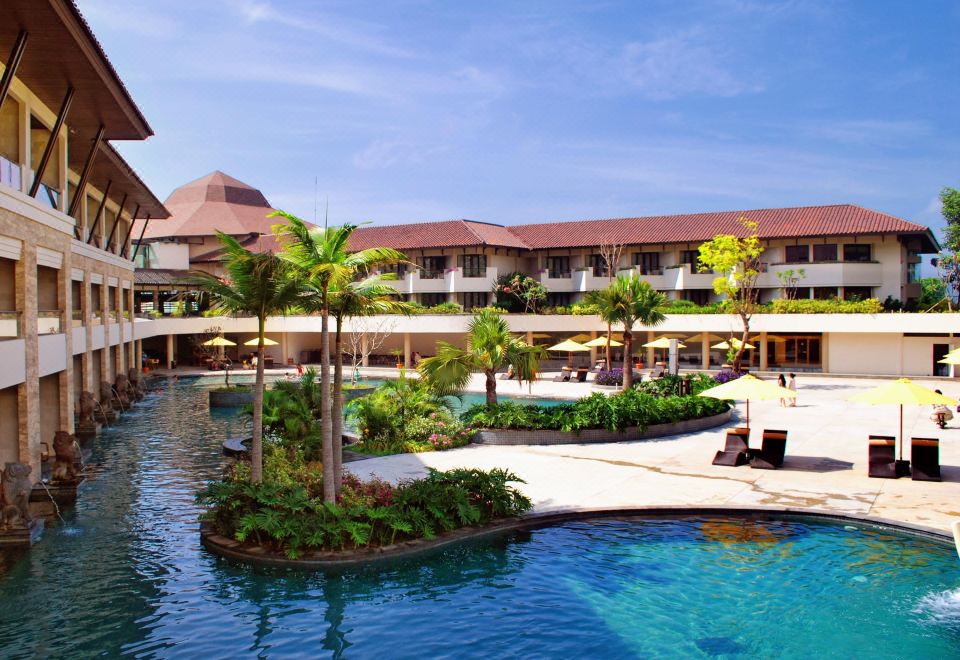 a large resort with a pool surrounded by lounge chairs and umbrellas , as well as a building in the background at The Singhasari Resort Batu