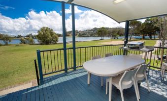 a wooden deck with a table and chairs , overlooking a green field and a lake at Discovery Parks - Ballina