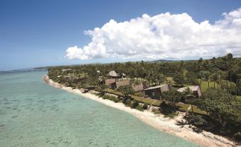 a tropical island with a sandy beach , clear blue water , and lush green vegetation under a cloudy sky at Shangri-La Yanuca Island, Fiji