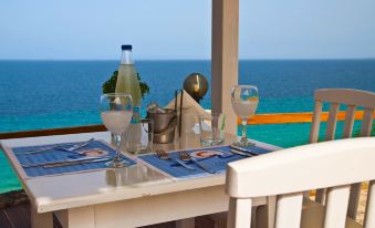 a table set for two with blue place mats , wine glasses , and a view of the ocean at Blue Bay Halkidiki