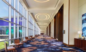 a long , empty hallway with large windows and carpeted flooring , decorated with circular lights and chandeliers at Omni Frisco at the Star