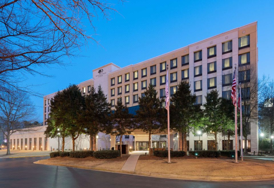 a large hotel building surrounded by trees , with the sun setting in the background at DoubleTree by Hilton Atlanta Airport