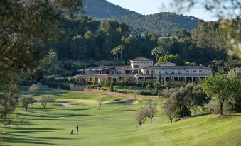 a golf course with a large building in the background , surrounded by trees and mountains at Sheraton Mallorca Arabella Golf Hotel