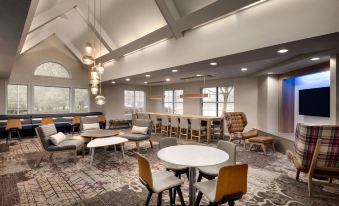 a spacious room with several white tables and chairs , a bar area , and large windows at Residence Inn West Springfield