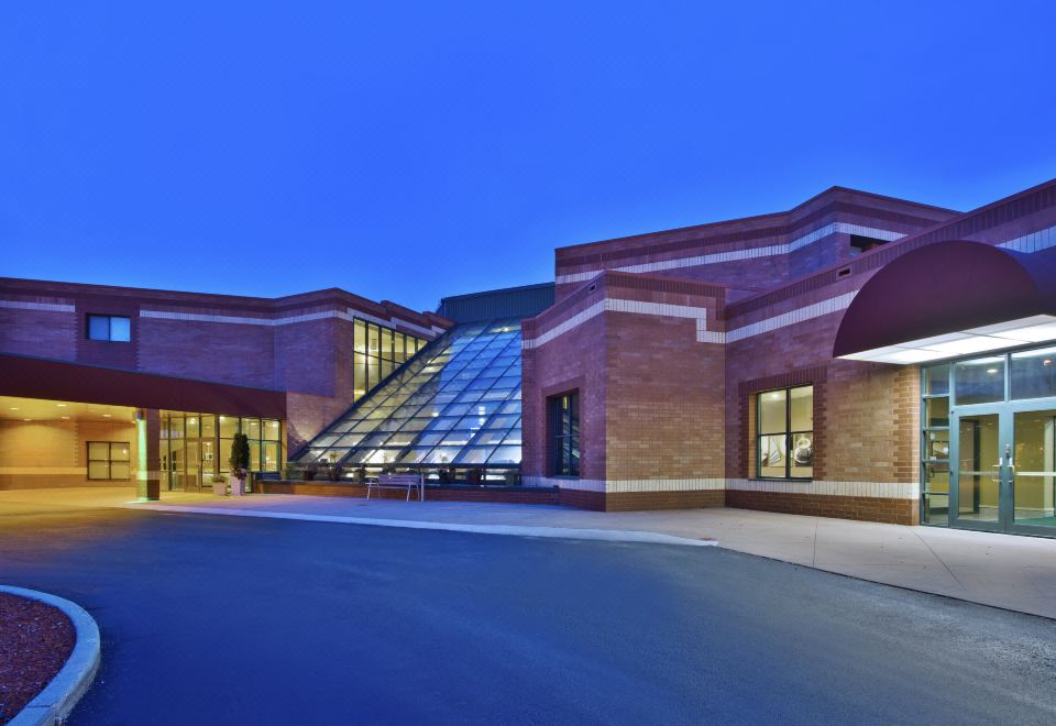 a large building with a glass facade is lit up at night , surrounded by trees and a parking lot at Holiday Inn Manitowoc