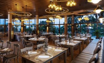 a large , well - lit restaurant with numerous dining tables and chairs arranged for a group of people at Sheraton Grand Adana