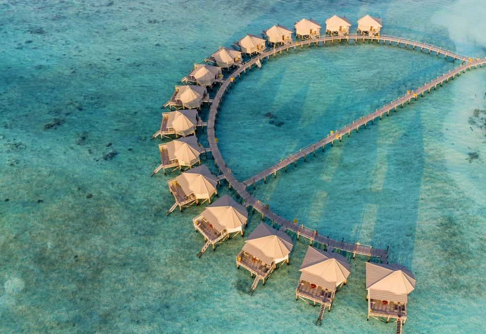 aerial view of a tropical island with multiple wooden cabins in the water , surrounded by clear blue water at Komandoo Island Resort & Spa