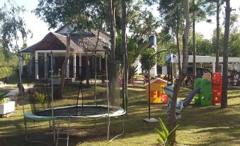 a playground with various equipment , including swings , a slide , and a trampoline , surrounded by a house at The Sanctuary