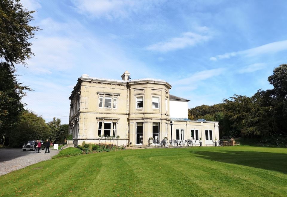 a large , old building surrounded by a grassy field , with people walking around the area at Cleatham Hall