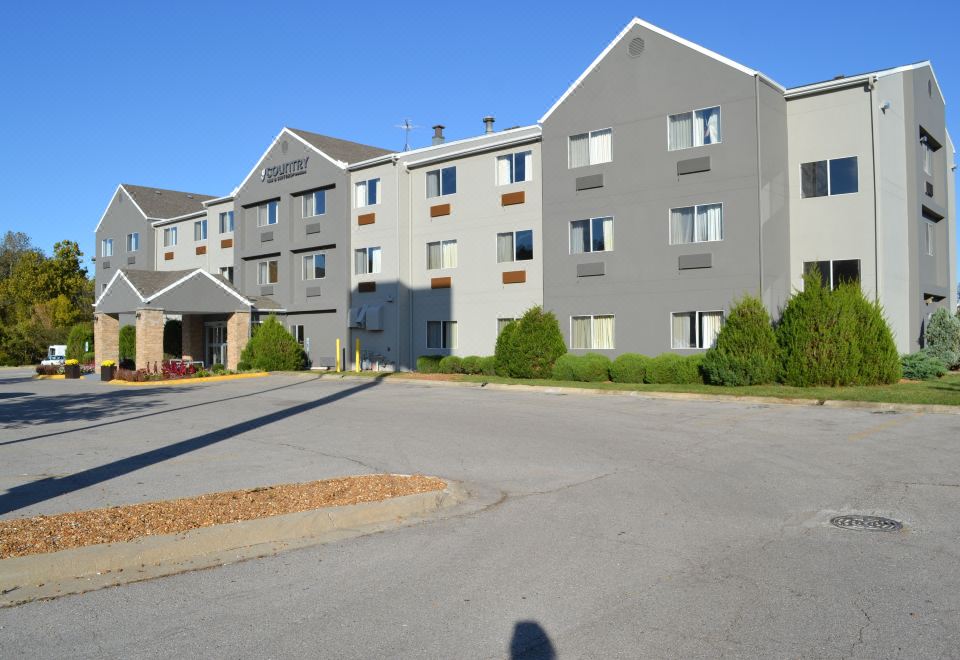 a large building with multiple windows and doors , surrounded by a parking lot with cars at Country Inn & Suites by Radisson, Fairview Heights, IL