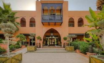 a beautiful pink building with an arched entrance , surrounded by lush greenery and potted plants at Tikida Golf Palace