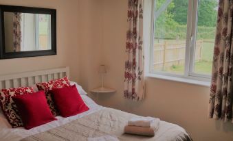 a well - decorated bedroom with a white bedspread , red pillows , and a window offering a view of the outdoors at Woodhouse Woodmancote