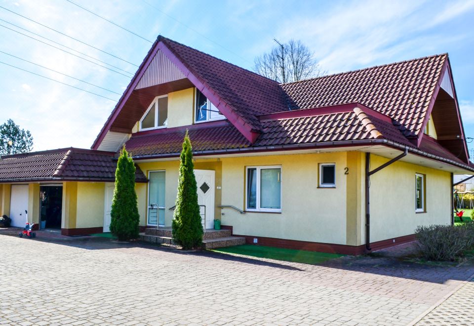 a yellow house with a red roof , surrounded by trees and parked cars on a sunny day at Kosmik